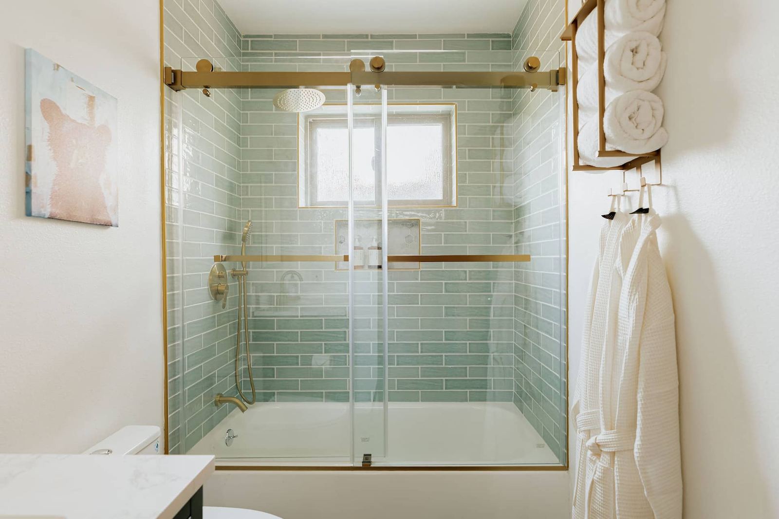 Remodeled bathroom with seafoam subway tile shower and gold fixtures